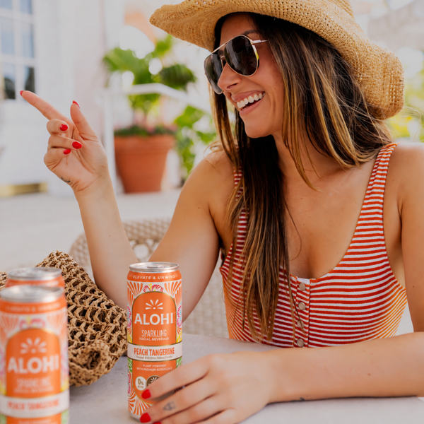 Woman in a sun hat at brunch with cans of Alohi Peach Tangerine